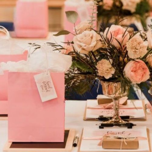 Pink Gift bag on table beside a bouquet of pink roses 
