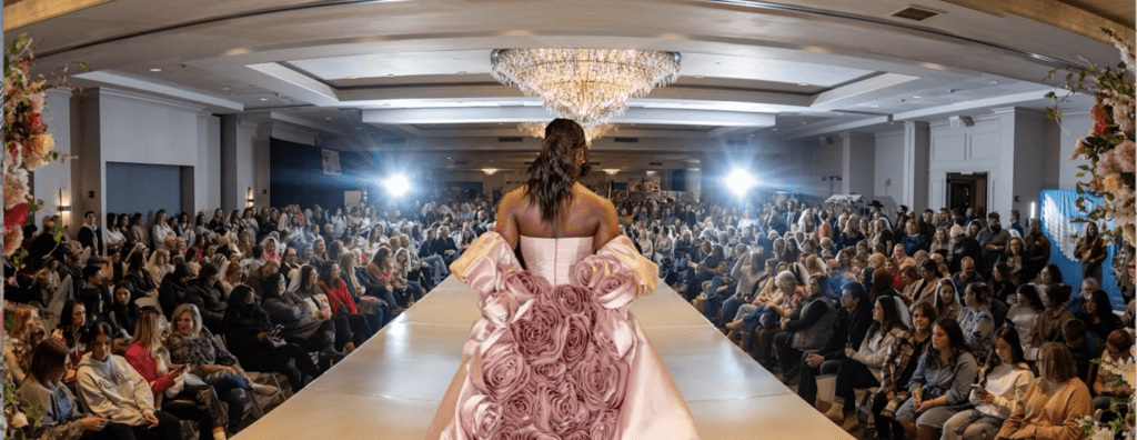 Fashion show runway bride in pink dress walking down the runway view is the back of the dress, looking into the audience